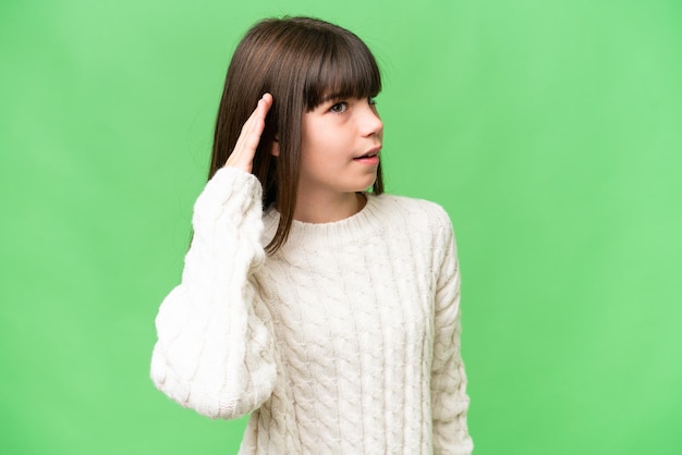 Niña caucásica sobre un fondo aislado escuchando algo poniendo la mano en la oreja