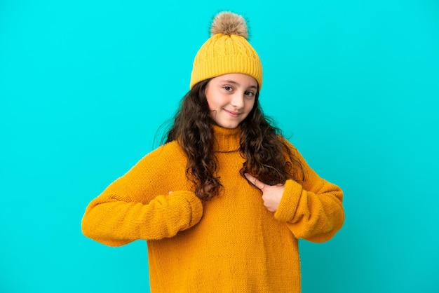 Niña caucásica con sombrero de invierno aislada de fondo azul con expresión facial sorpresa