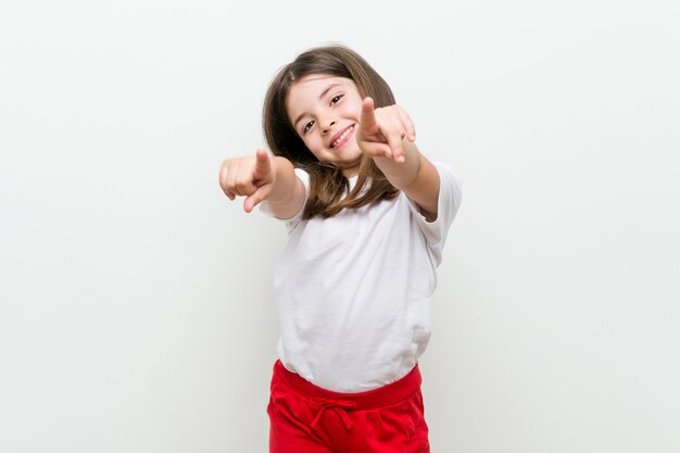 Niña caucásica sonrisas alegres apuntando al frente.