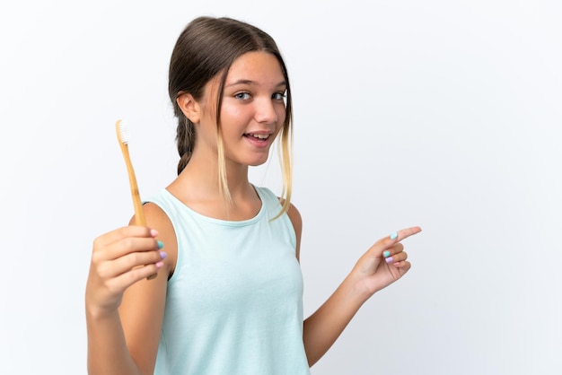 Foto niña caucásica sosteniendo un cepillo de dientes aislado de fondo blanco sorprendida y señalando con el dedo hacia un lado