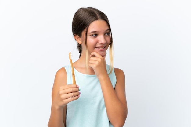 Niña caucásica sosteniendo un cepillo de dientes aislado sobre fondo blanco pensando en una idea y mirando de lado