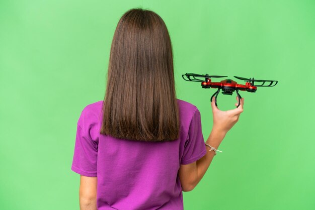 Niña caucásica sosteniendo un dron sobre un fondo aislado en posición trasera