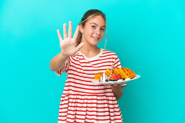 Niña caucásica sosteniendo gofres aislados en fondo azul contando cinco con los dedos