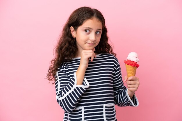 Niña caucásica sosteniendo un helado aislado de fondo rosa con dudas y pensando