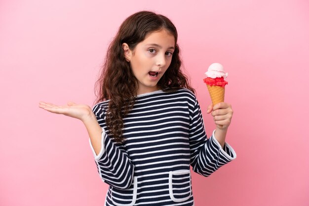 Niña caucásica sosteniendo un helado aislado de fondo rosa con una expresión facial sorprendida