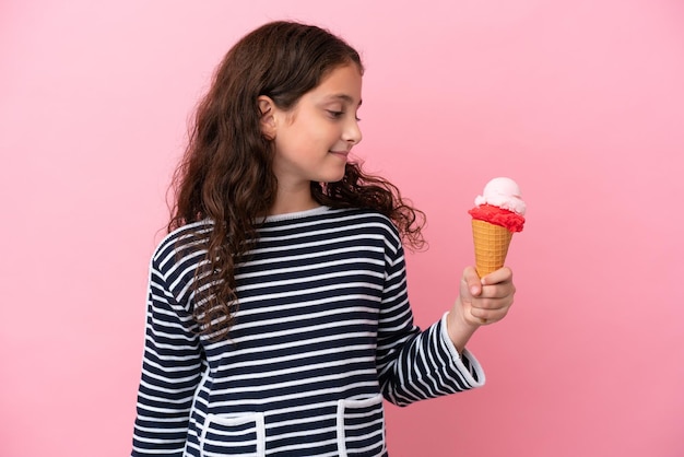 Niña caucásica sosteniendo un helado aislado en un fondo rosa mirando hacia un lado