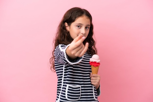 Niña caucásica sosteniendo un helado aislado sobre fondo rosa haciendo gesto de dinero