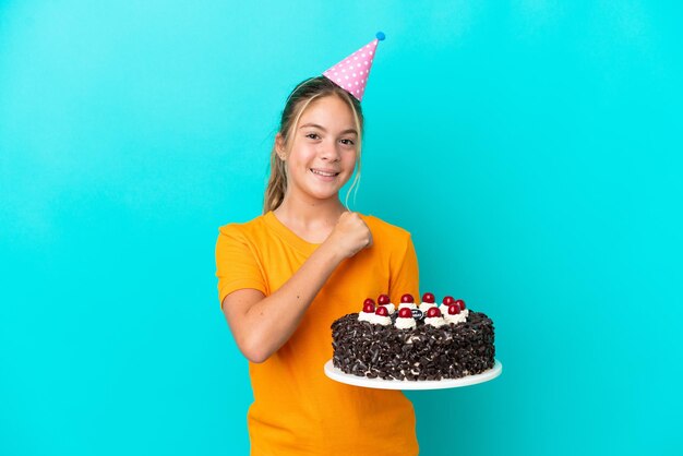 Niña caucásica sosteniendo pastel de cumpleaños aislado de fondo azul celebrando una victoria