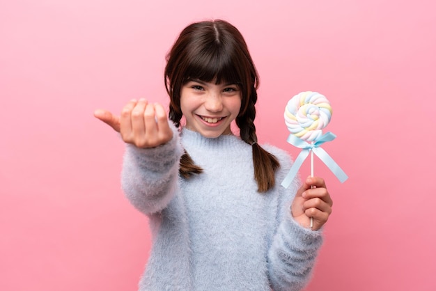 Niña caucásica sosteniendo una piruleta invitando a venir con la mano Feliz de que hayas venido