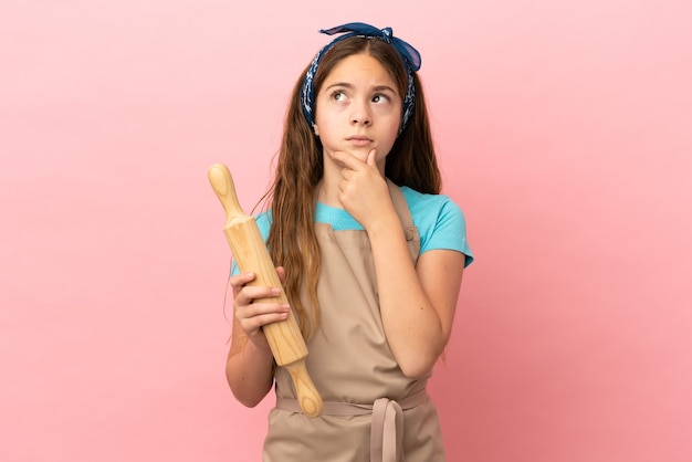 Niña caucásica sosteniendo un rodillo aislado sobre fondo rosa con dudas