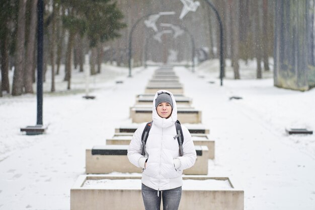 Niña caucásica vestida de chaqueta blanca disfrutando de nevadas en el parque