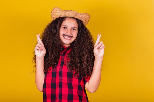 Niña caucásica vestida como un niño con ropa de fiesta, con los dedos cruzados, animando, deseando, deseando, esperanzados, festivales en mayo, junio y julio.