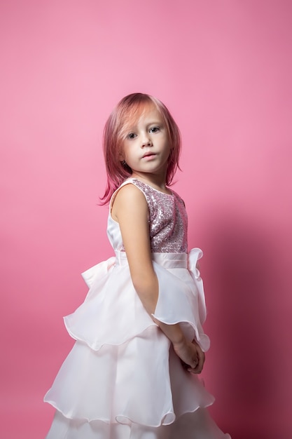 Foto niña caucásica en un vestido de fiesta con lentejuelas posando sobre un fondo rosa mirando a la cámara