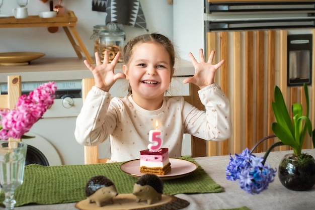 La niña celebra el pastel de cumpleaños con el número cinco que el bebé muestra con las manos 5