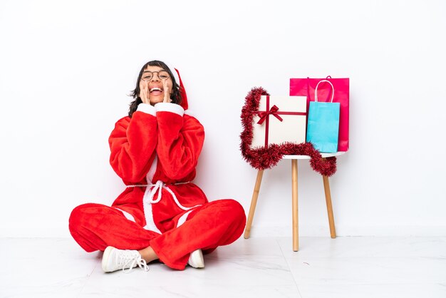 Niña celebrando la Navidad sentada en el suelo aislado en blanco bakcground gritando y anunciando algo