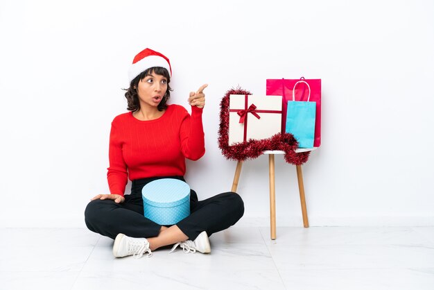 Niña celebrando la Navidad sentados en el suelo aislado en blanco bakcground apuntando hacia afuera