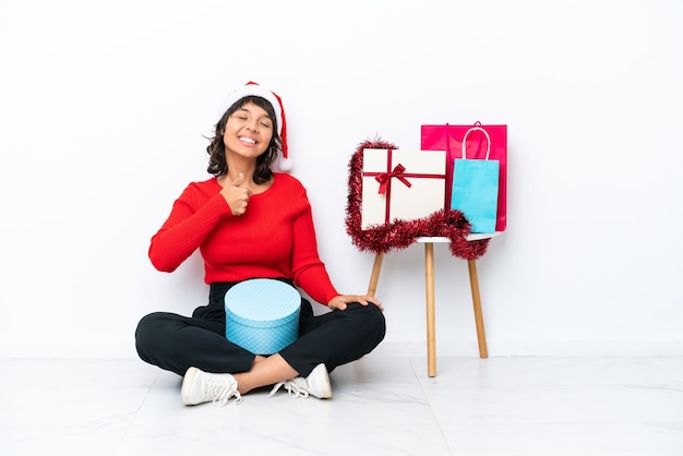 Niña celebrando la Navidad sentados en el suelo aislado en blanco bakcground dando un pulgar hacia arriba gesto