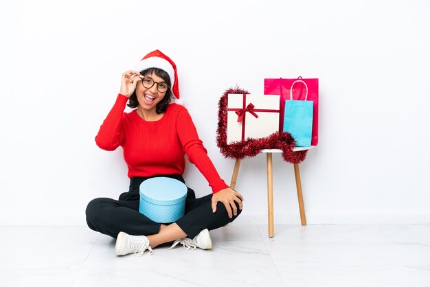 Niña celebrando la Navidad sentados en el suelo aislado en blanco bakcground con gafas y feliz