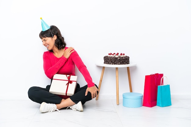 Niña celebrando su cumpleaños sentada en el suelo aislado sobre fondo blanco que sufre de dolor en el hombro por haber hecho un esfuerzo