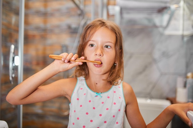 Niña cepillarse los dientes con cepillo de dientes de madera ecologe en el baño.