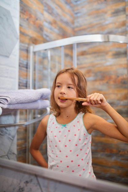 Niña cepillarse los dientes con cepillo de dientes de madera ecologe en el baño.