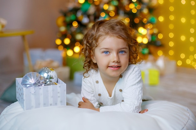 Niña cerca del árbol de Navidad jugando con juguetes de Navidad