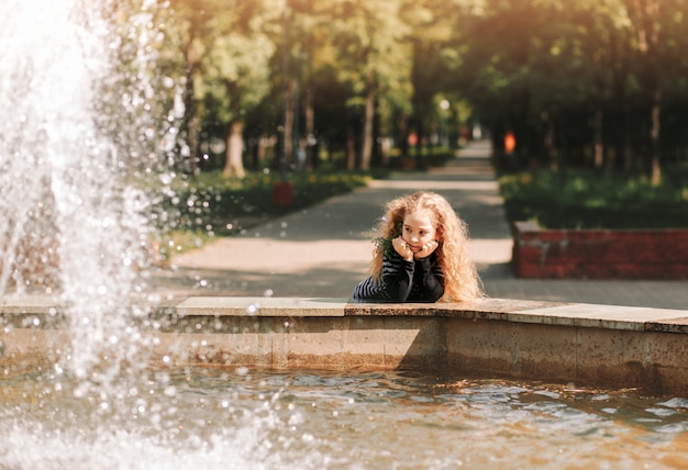 Niña cerca de la fuente en el parque en verano