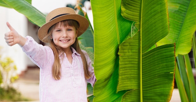 Niña de cerca con palmeras en el fondo. Ella está mostrando un pulgar hacia arriba. foto de alta calidad