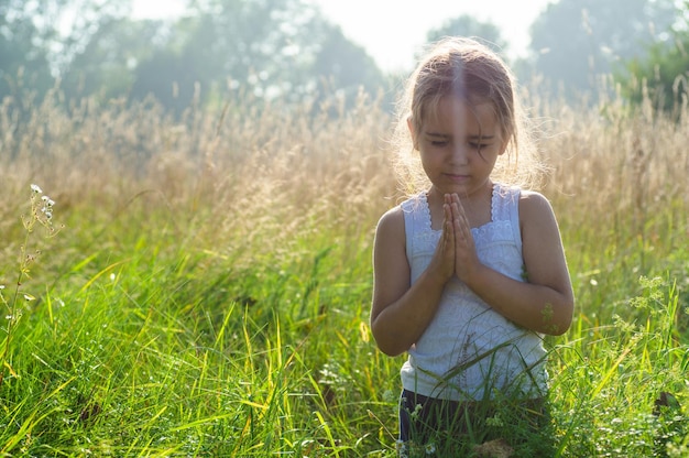 La niña cerró los ojos rezando al aire libre Las manos dobladas en el concepto de oración por la fe, la espiritualidad y la religión Concepto de sueños de esperanza de paz