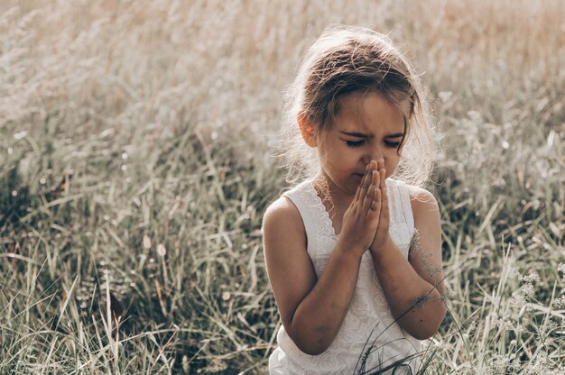 La niña cerró los ojos, rezando al aire libre, con las manos juntas en concepto de oración por la fe, la espiritualidad y la religión. Paz, esperanza, concepto de sueños.