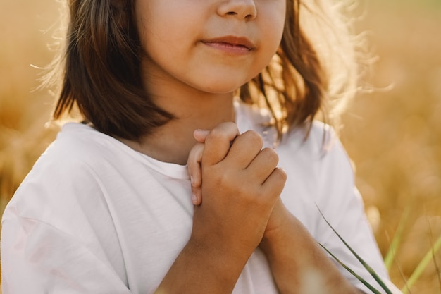 Niña cerró los ojos, rezando en un campo de trigo. Manos juntas en oración. Concepto de religión