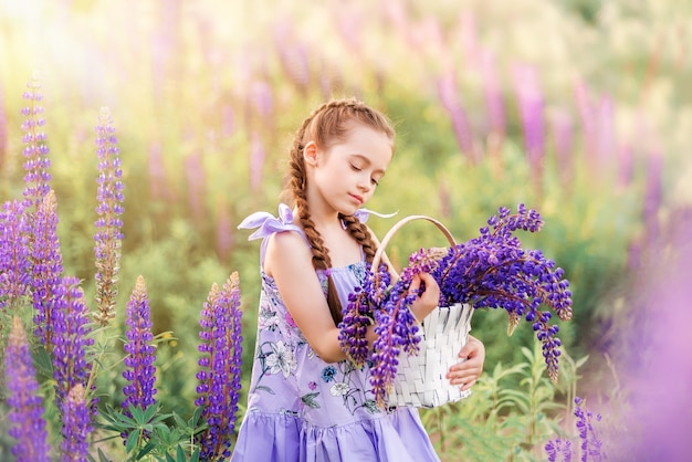 Niña con una cesta de flores de color púrpura. Un niño en la naturaleza. Niña en un campo con flores