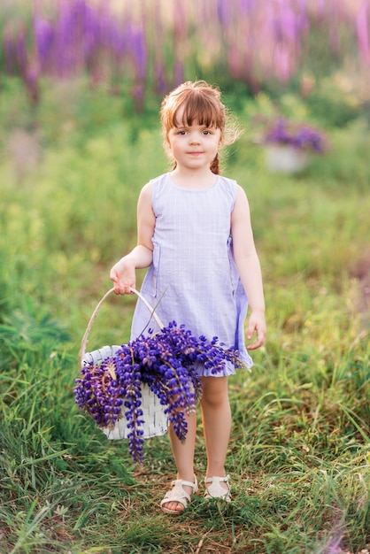 Niña con una cesta de flores de color púrpura. Niño en la naturaleza