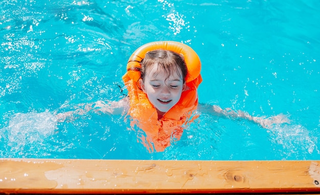 Una niña con un chaleco salvavidas naranja nada en la piscina.