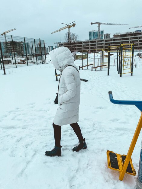 Una niña con una chaqueta blanca camina en una capucha en el invierno nevado en el calor del país del norte en un cálido