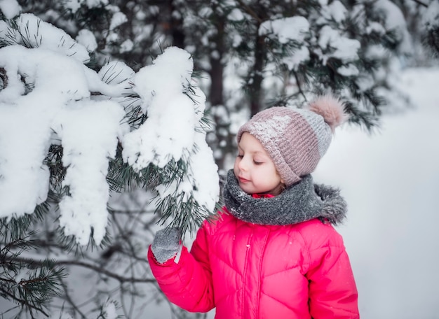 Una niña con una chaqueta brillante juega en el bosque nevado de invierno.