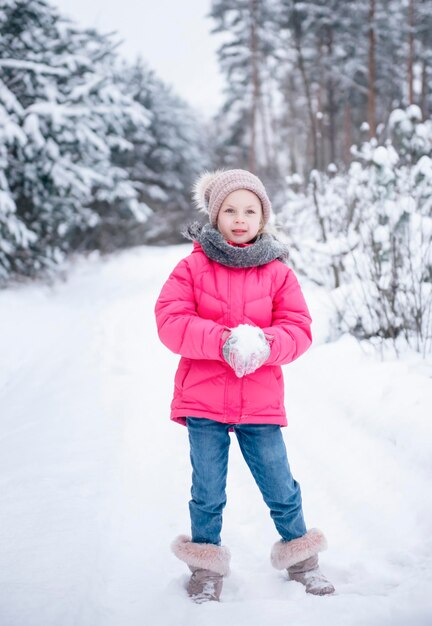 Una niña con una chaqueta brillante juega en el bosque nevado de invierno.