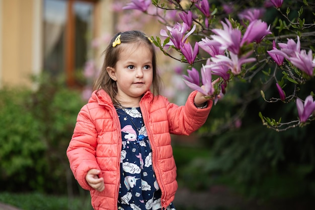 Niña con chaqueta rosa disfrutando de un agradable día de primavera cerca del árbol floreciente de magnolia Actividades de primavera