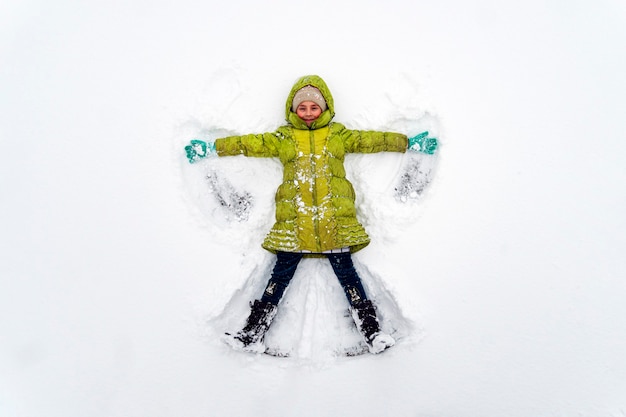 Una niña con una chaqueta verde juega en la nieve en un clima helado. La vista desde arriba. Pequeño ángel. Hermosa niña en el parque de invierno. Actividades al aire libre para niños de invierno.