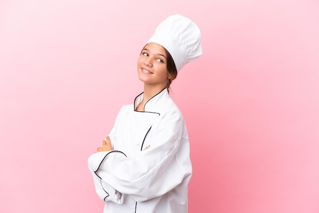 Niña chef caucásica aislada sobre fondo rosa con los brazos cruzados y feliz