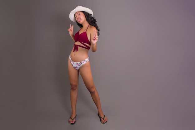 Niña china en bikini y sombrero sacando la lengua con expresión burlona divertida