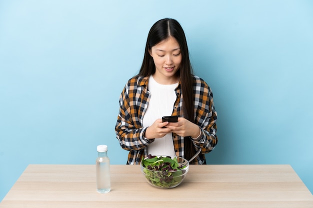 Niña china comiendo una ensalada enviando un mensaje con el móvil