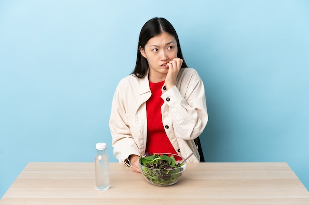 Niña china comiendo una ensalada está un poco nerviosa