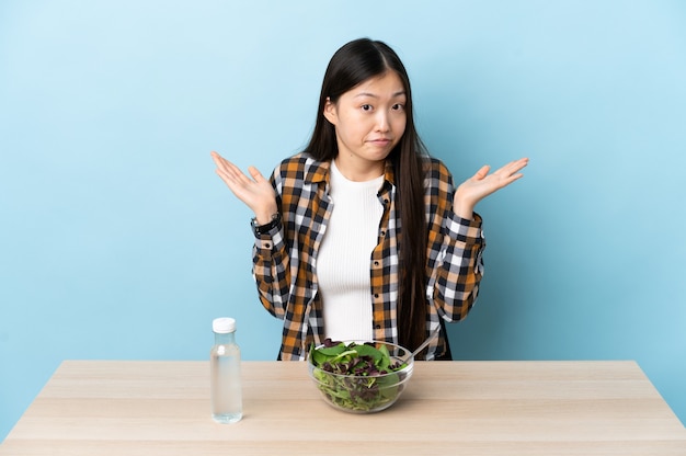 Niña china comiendo una ensalada haciendo gesto de dudas