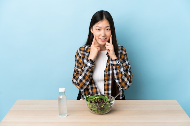 Niña china comiendo una ensalada sonriendo con una expresión feliz y agradable