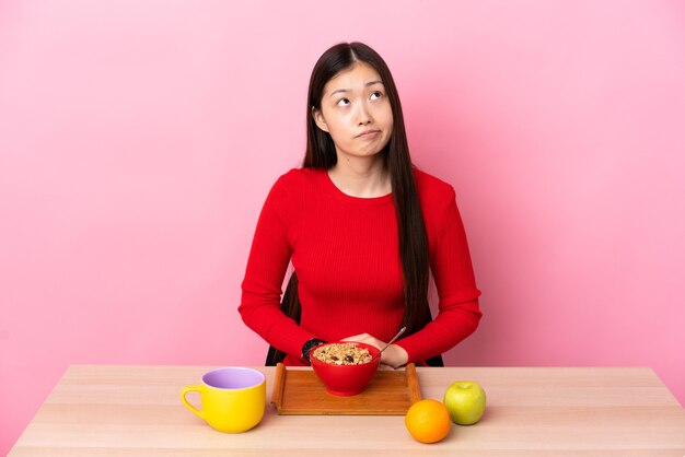 Niña china desayunando en una mesa y mirando hacia arriba