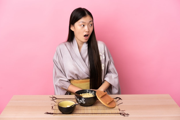 Niña china con kimono y comiendo fideos haciendo gesto de sorpresa mientras mira hacia un lado