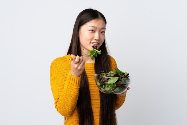 Niña china sobre fondo blanco aislado sosteniendo un plato de ensalada con expresión feliz