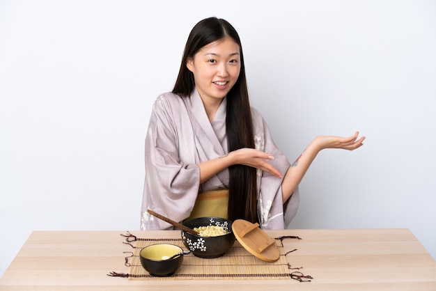 Niña china vistiendo kimono y comiendo fideos extendiendo las manos hacia un lado para invitar a venir