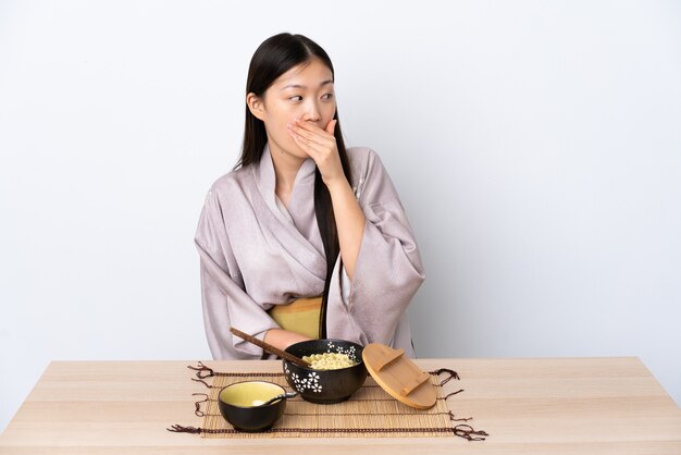 Niña china vistiendo kimono y comiendo fideos haciendo gesto de sorpresa mientras mira hacia un lado